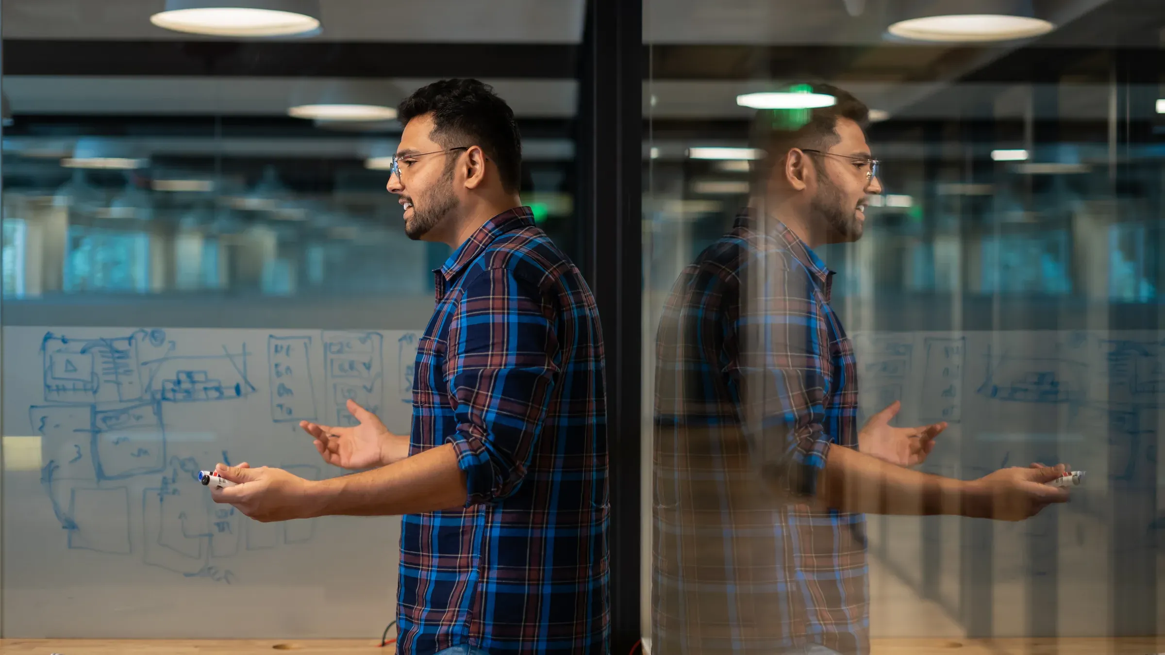 Ayushman Dash explaining a diagram at a glass whiteboard, his reflection beside him